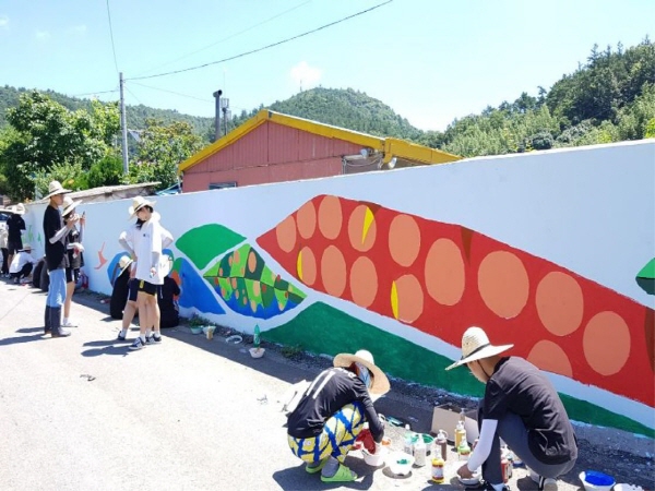 봉사에 참여한 미술동아리 학생들이 한쪽에선 흰벽에 벽화를 그리고 있고, 다른 한쪽에선 페인트통을 만지고 있는 모습