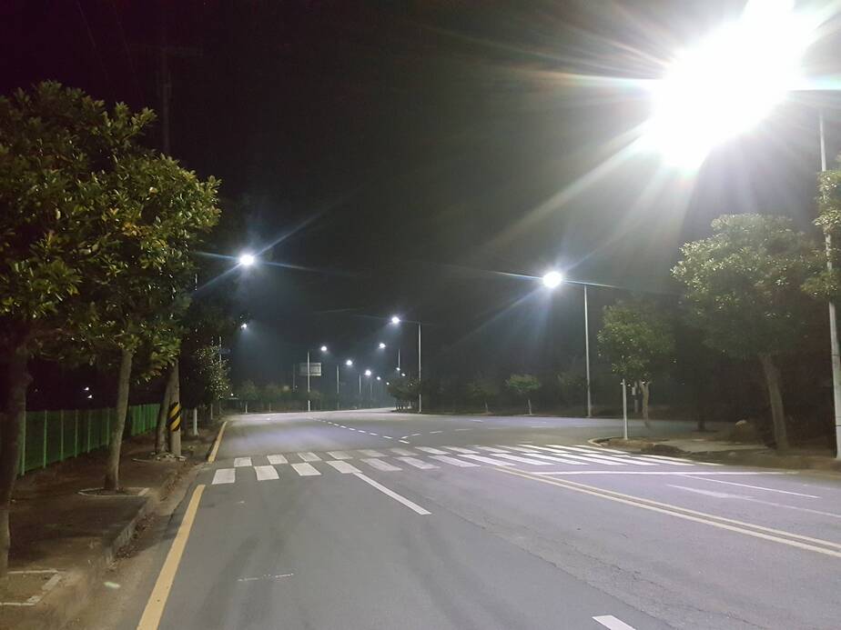 밤에 왕복 4차선 도로를 찍은 사진. 가로등이 밝게 비쳐져서 도로가 환하게 보임. 도로 가에는 가로수가 심겨져 있음.