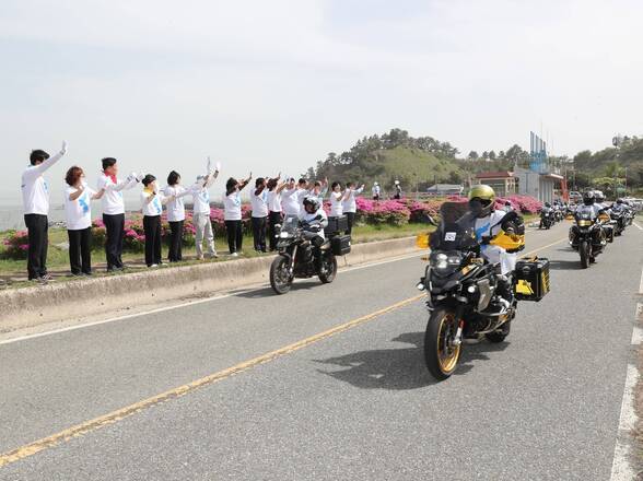 통일기원 퍼레이드중인 오토바이 행렬과 길가에서 손을 흔들고 있는 군민들 사진(크게보기)