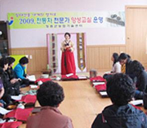 한 여성이 한복을 입고 양성교육을 하며 다른 사람들은 경청하는 모습