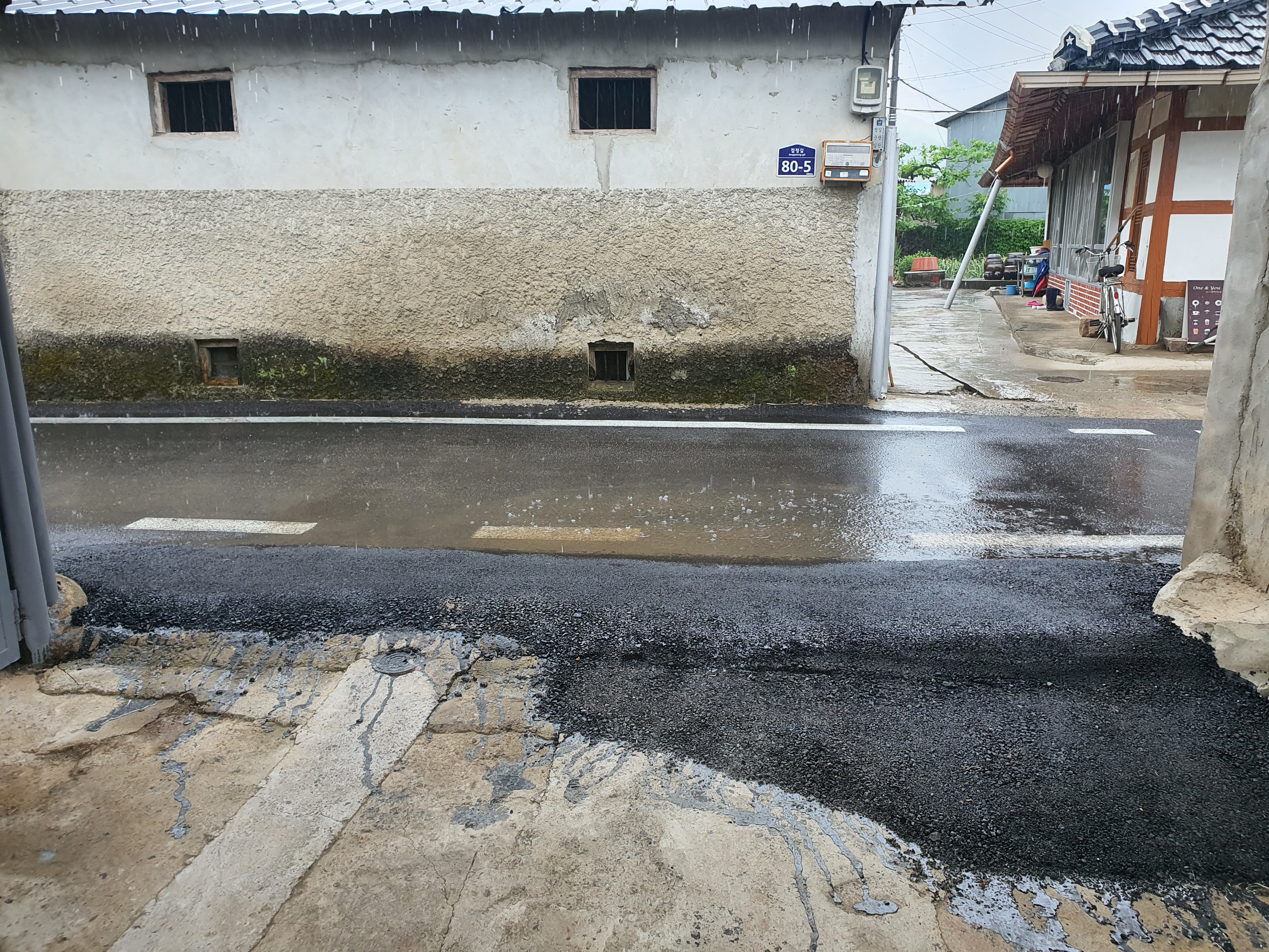 공사완료후 많은 비가 와도 유입되지 않음 -비가 많이 와서 처마 밑으로 빗물이 떨어지고 있고 도로명이 붙은 돌벽이 있다.